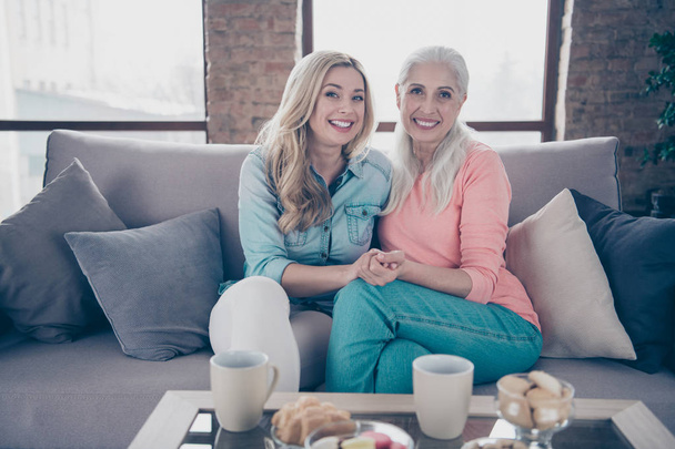 Close up photo two people she her ladies rumours mom granddaughter child granny hot beverage tea table hugging hold hands wear casual domestic clothes sit comfy couch divan flat house indoors - Foto, Imagen