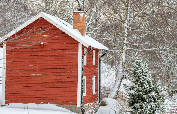 uma casa vermelha com neve no telhado e floresta no fundo
 - Foto, Imagem
