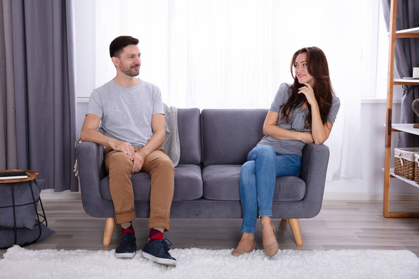 Happy Young Couple Sitting On Sofa Looking At Each Other - Фото, зображення