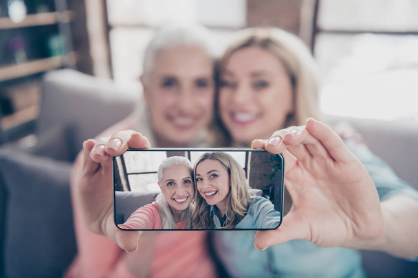 Close up photo two beautiful she her ladies funky granny granddaughter relatives mom mommy make take selfies toothy telephone hands arms blurred picture sit couch divan sofa house indoors - Fotoğraf, Görsel