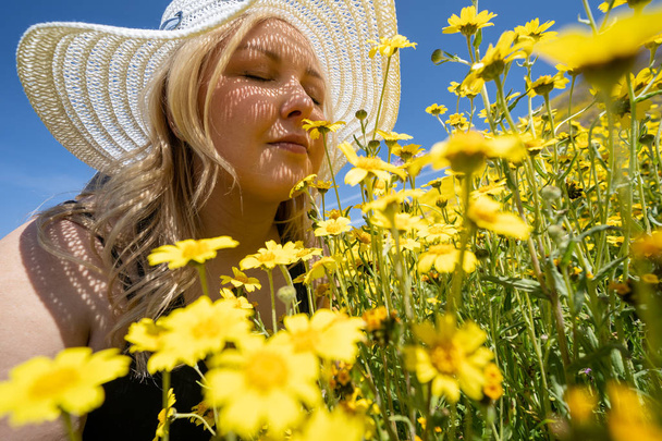 Femme blonde portant un chapeau blanc de paille sentant un champ de jaune
  - Photo, image