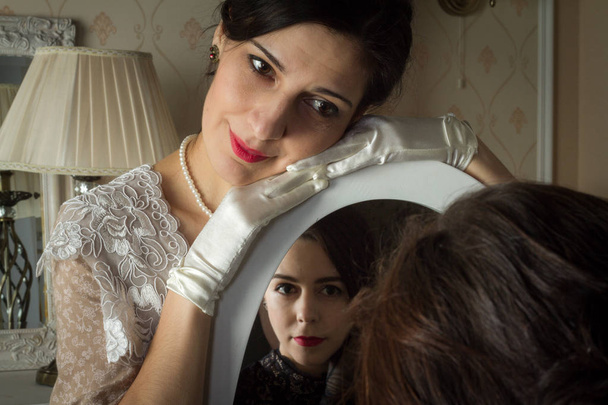 Δύο νεαρές γυναίκες σε vintage φορέματα κοιτάν ο ένας τον άλλο μέσα από έναν καθρέφτη, μια αντανάκλαση της αγάπης. Προστέθηκε ένα μικρό σιτάρι, απομίμηση της φωτογραφίας φιλμ - Φωτογραφία, εικόνα
