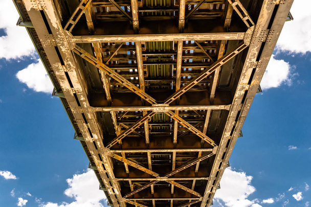 Μεταλλική κατασκευή πλέγματος μιας σιδηροδρομικής γέφυρας σε φόντο γαλάζιου ουρανού με λευκά σύννεφα. - Φωτογραφία, εικόνα