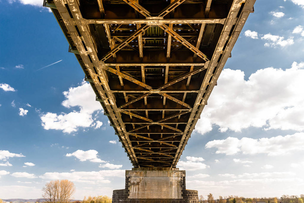 Μεταλλική κατασκευή πλέγματος μιας σιδηροδρομικής γέφυρας σε φόντο γαλάζιου ουρανού με λευκά σύννεφα. - Φωτογραφία, εικόνα