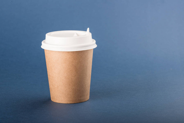 Kraft disposable cup with white cap on a blue background - Valokuva, kuva