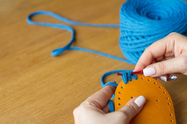 Manos de una mujer joven tejer ganchillo de hilo azul sobre una superficie de madera clara. Iniciar una nueva bolsa de hilo
. - Foto, Imagen