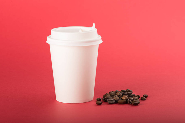 White disposable paper cup with white cap and coffee beans on a red background - Valokuva, kuva