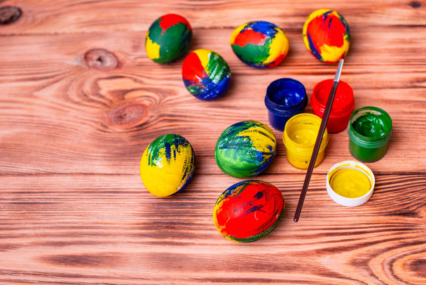 Пасхальные разноцветные яйца, краски и кисти на столе. Подготовка к празднику
 - Фото, изображение