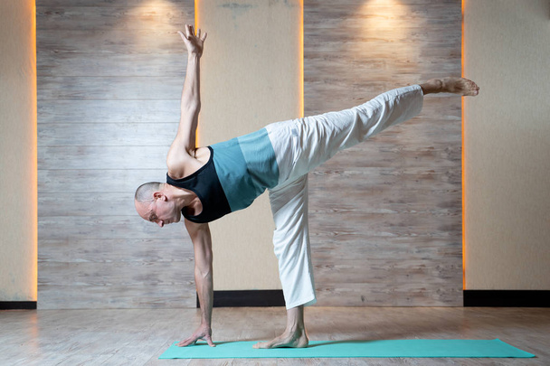 Athletic man standing leg doing yoga on blue mat. - Foto, imagen