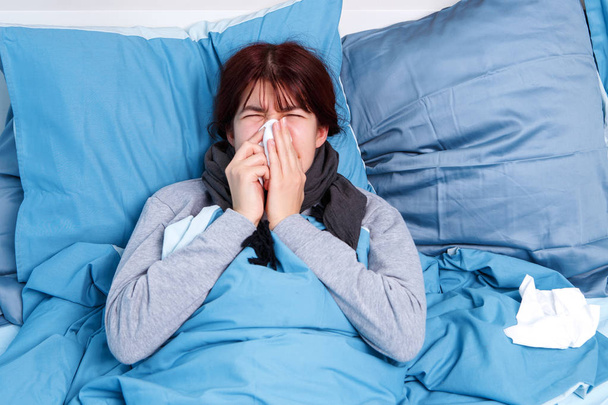 Foto de chica morena enferma sonándose la nariz en una bufanda de papel acostada en la cama
. - Foto, Imagen