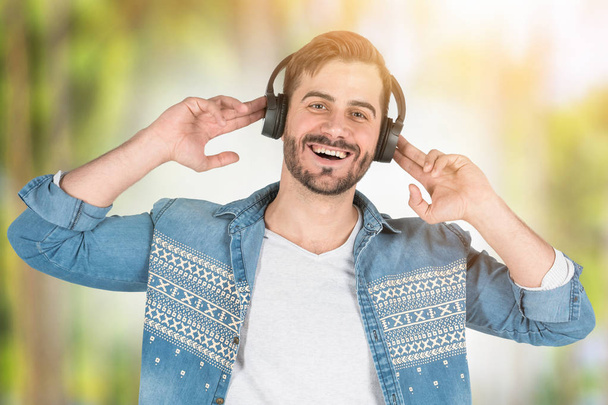 Happy man in headphones in blurred park - Фото, изображение