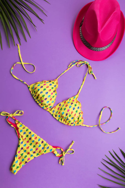 Summer background with palm leaves, pink fashion hat and bikini on violet or purple background, travel and vacations concept, top view - Photo, Image
