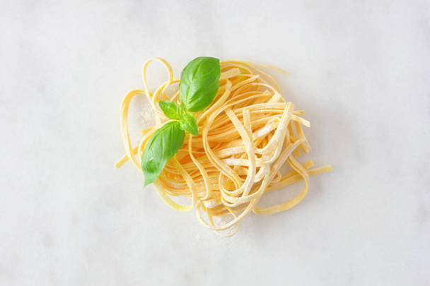 Nest of fresh linguine pasta with basil. Top view against a white marble background. - Фото, изображение
