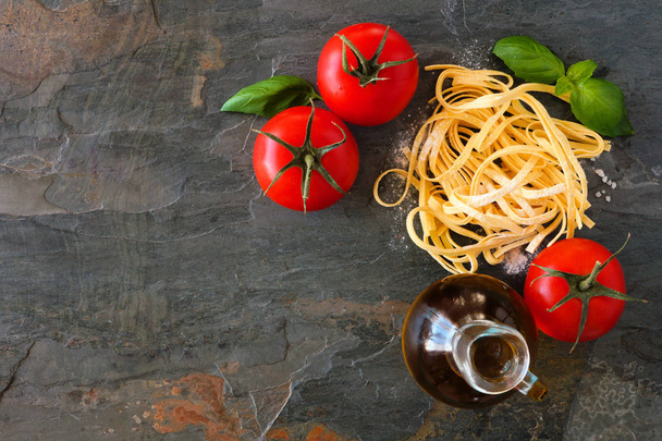 Pasta ingredients including fresh linguine, tomatoes, olive oil and basil. Top view against a slate background. - Foto, imagen