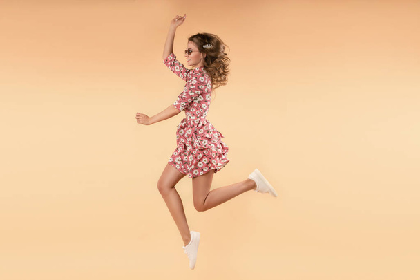 Pembe çiçek elbise atlama ve stüdyoda gülüyor kız - Fotoğraf, Görsel