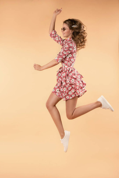 Menina de vestido floral rosa pulando e rindo em estúdio
 - Foto, Imagem