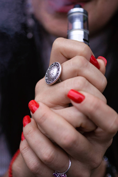 Fehér nő piros körömmanikűrrel és antik gyűrűvel az ujján kis gőzt hordoz. Dohányzó alternatív vay. A nő sűrű füstöt lélegez ki. Élet cigaretta nélkül. Nő-szívó. Kis méretű e-cigaretta. - Fotó, kép