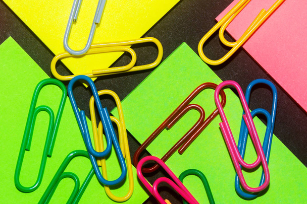 Συνδετήρες σε πολύχρωμα διαφορετικά αυτοκόλλητα γραφείου σε μαύρο χαρτί. - Φωτογραφία, εικόνα