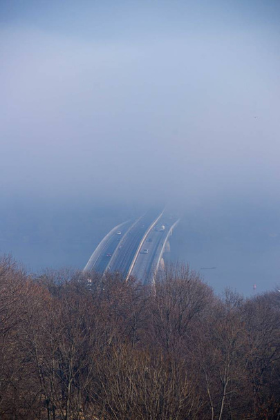 Niebla otoñal y puente de acero fluvial con tren subterráneo sobre fondo borroso. Bosque en primer plano.  - Foto, imagen