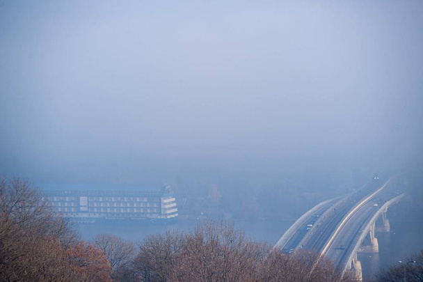 Осенний туман и речной стальной мост с поездом метро на размытом фоне. Большой лодочный отель в реке. Лес на переднем плане.  - Фото, изображение