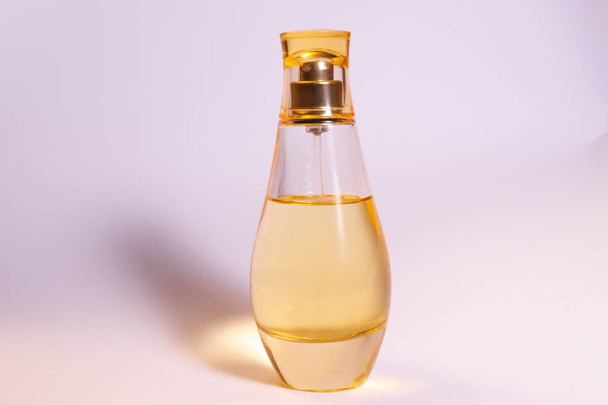 Teplá žlutá barva sklo parfum láhev na bílo-fialové pozadí.  - Fotografie, Obrázek
