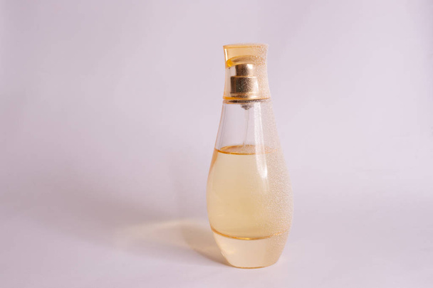 Bottiglia da parfum in vetro di colore giallo caldo con neve artificiale su fondo bianco-viola. Vista da vicino. - Foto, immagini