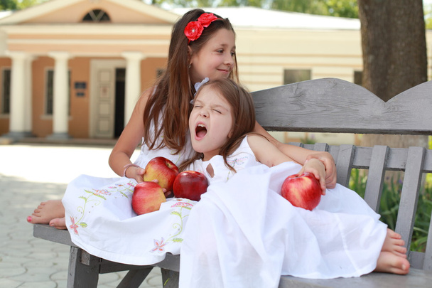 Lovely girls with basket of red apples on a bench - Zdjęcie, obraz