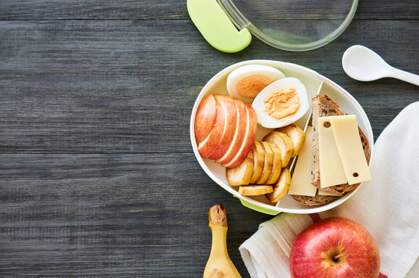 Lunch box with sandwich, egg and fresh fruit on a wooden table                                - Photo, Image