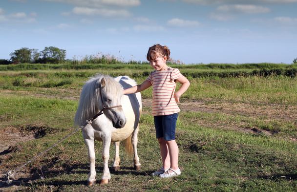klein meisje en witte pony paard op de weide - Foto, afbeelding