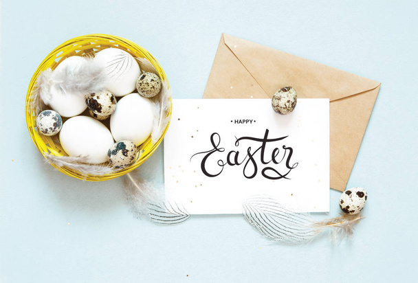 Inscription Happy Easter, kraft envelope. Easter composition with easter eggs and feathers. Flat lay, top view. - 写真・画像