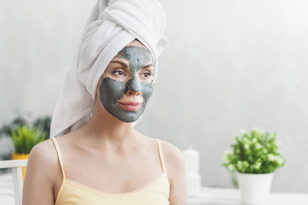 Face Skin care. Attractive Young Woman Wrapped in Bath Towel, applying clay mud mask to face. Skin care concept. Girl taking care of complexion. Beauty treatments - Photo, image