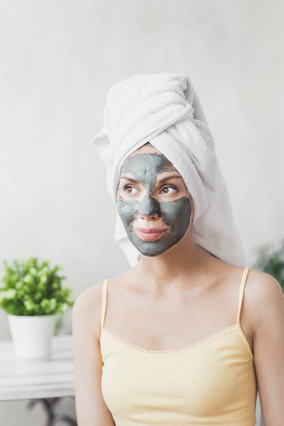 Face Skin care. Attractive Young Woman Wrapped in Bath Towel, applying clay mud mask to face. Skin care concept. Girl taking care of complexion. Beauty treatments - Photo, image