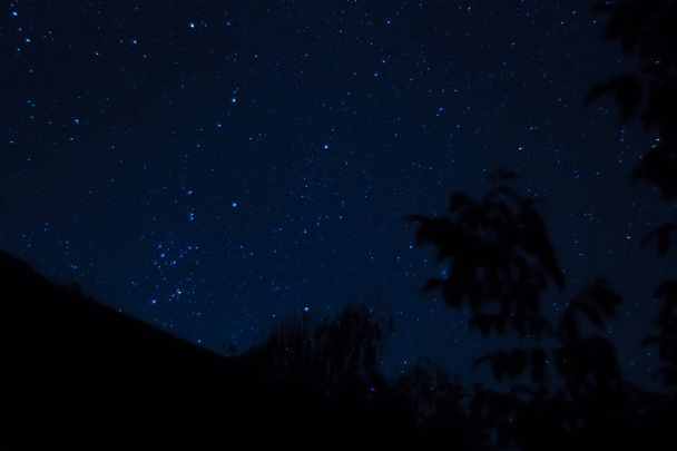 長時間露光夜の写真。手前に屋根のある星がたくさんあります。街から遠く. - 写真・画像