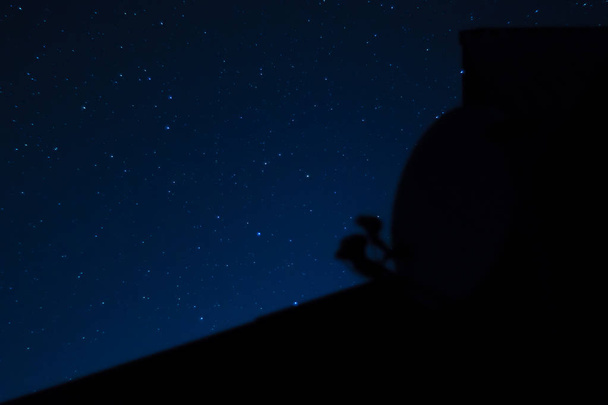 Foto nocturna de larga exposición. Un montón de estrellas con techo y antena parabólica en primer plano. Lejos de la ciudad. - Foto, imagen
