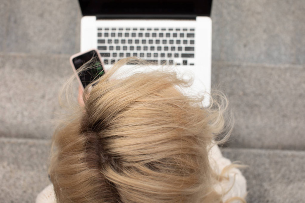 Jovem mulher bonita sentada com laptop tendo coffee break nas escadas. Menina caucasiana trabalhando com notebook ao ar livre
. - Foto, Imagem