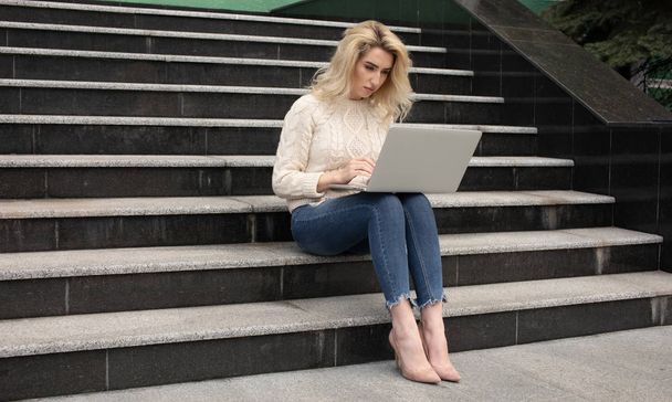 Young attractive businesswoman sitting on the stairs and using modern laptop - Фото, зображення
