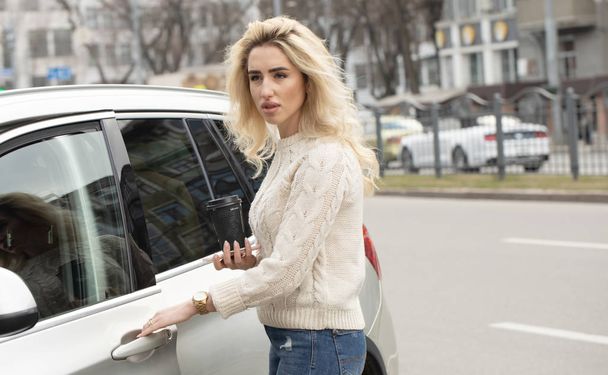 Beautiful young woman standing and opening the door in her car outdoors - Фото, изображение
