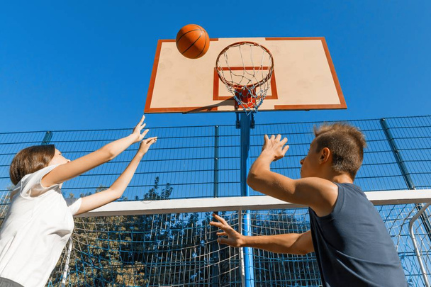 Streetball basketball game with two players, teenagers girl and boy with ball, outdoor city basketball court. - Photo, image