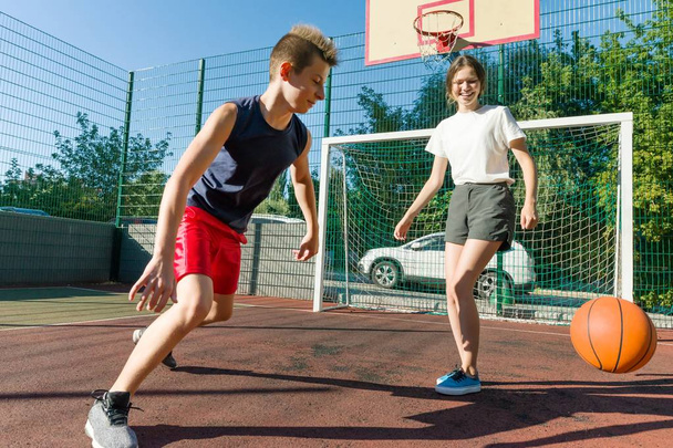 Streetball basketball game with two players, teenagers girl and boy, morning on basketball court - 写真・画像