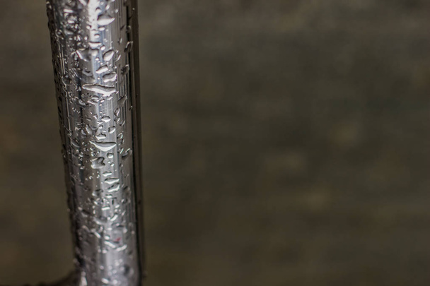 wet gray metal pipe plumbing object on dark blurred unfocused background with empty copy space for text - Foto, Imagen