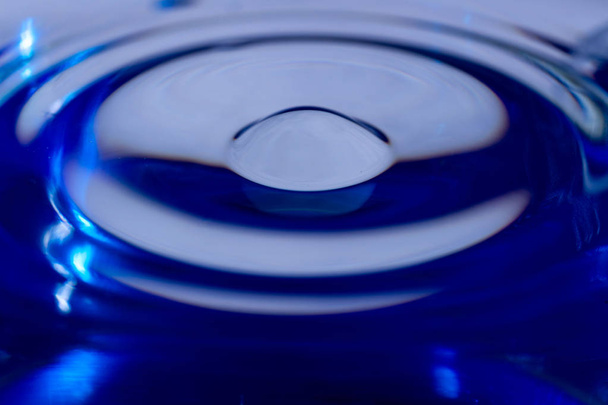 Waves on water surface in blue glass. Drop falling and splashing in water. Soft focus photo.  - Photo, image