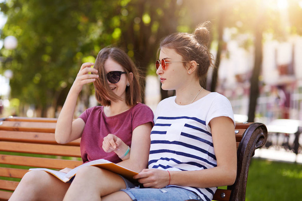 Happy cheerful girls are in the park to enjoy summer atmosphere and read latest news in world. Young beautiful friends give funny comments to each photo and laugh loudly. Friendship concept. - Foto, afbeelding