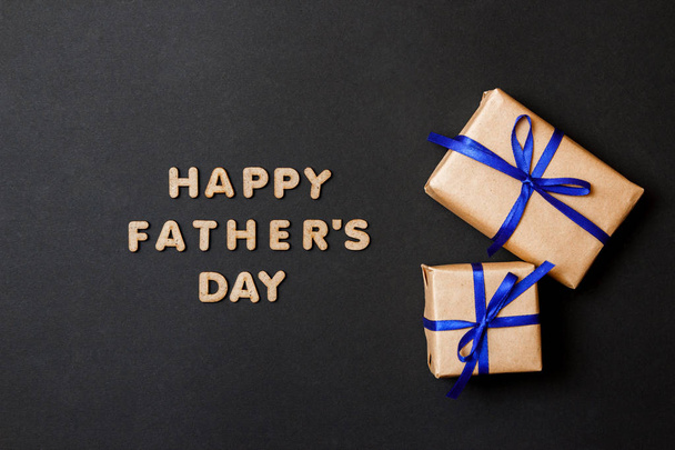 Grußkarte zum Vatertag. zwei handwerkliche Geschenke mit blauen Bändern auf schwarzem Hintergrund. - Foto, Bild