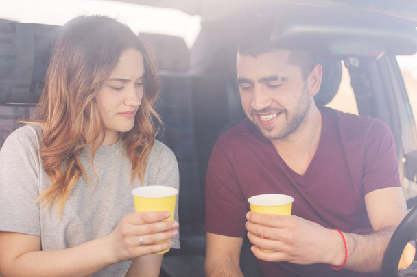 Attractive female and unshaven male couple have coffee break in auto, reach destination wih high speed. Happy family spend time together, travel on weekend, enjoying cool vocation. Travelling concept. - 写真・画像