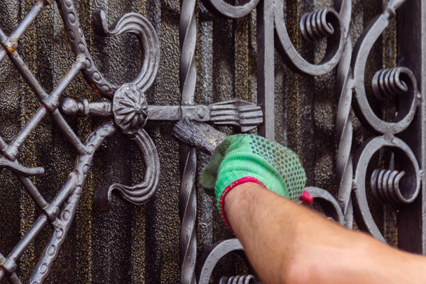 Een man schildert een poort met vervalste elementen. Op zijn hand is een groene handschoen, bij de elleboog van een schampschot. De hand bevindt zich rechts van het frame. - Foto, afbeelding