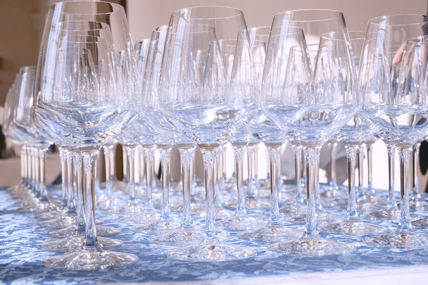Grupo de copas de vino de cristal, arregladas en filas ordenadas, preparaciones finales antes de empezar una cata de vinos vernissage
. - Foto, Imagen