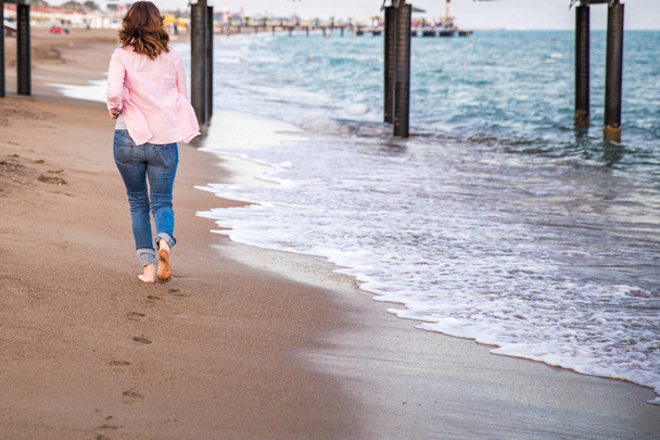 Woman wearing jeans running at sunet on the beach sand - Photo, Image