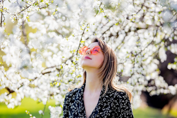Young girl in a sunglasses stay near a flowering tree - Zdjęcie, obraz