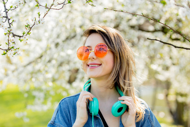 girl in a denim jacket and headphones near a flowering tree - Фото, изображение