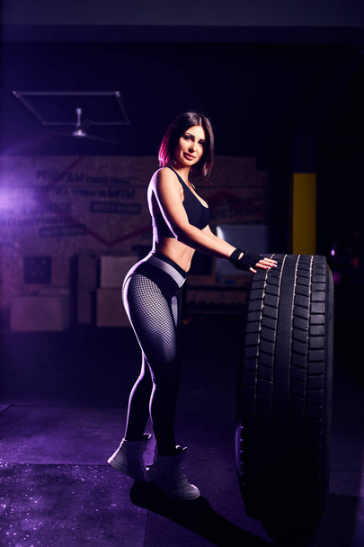 Attractive fit middle age woman athlete posing with a huge tire in the gym. Crossfit woman with big tire - Photo, image